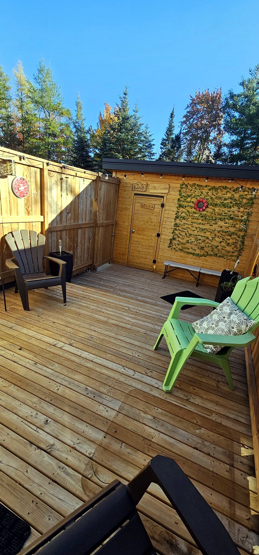 Wide view of the wooden terrace with lounge chairs and the sauna building under tall trees